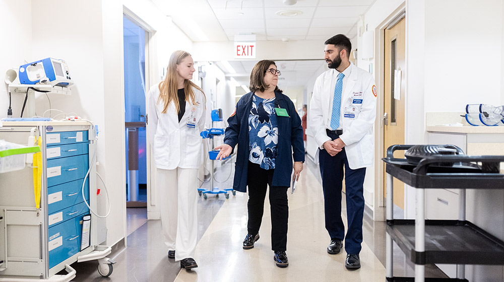 Two medical students wearing white coats walking down a hospital hallway with a Chaplain